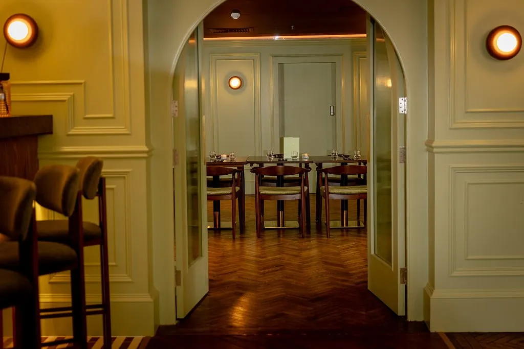 An inviting view through an arched doorway reveals a warmly lit dining room with classic wooden furniture and paneled walls.
