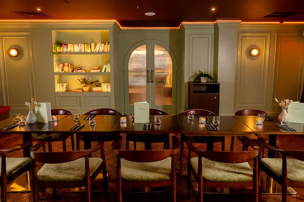 A warm and inviting restaurant dining area features sage green walls, dark wood furniture, and ambient lighting, creating a sophisticated and cozy atmosphere.