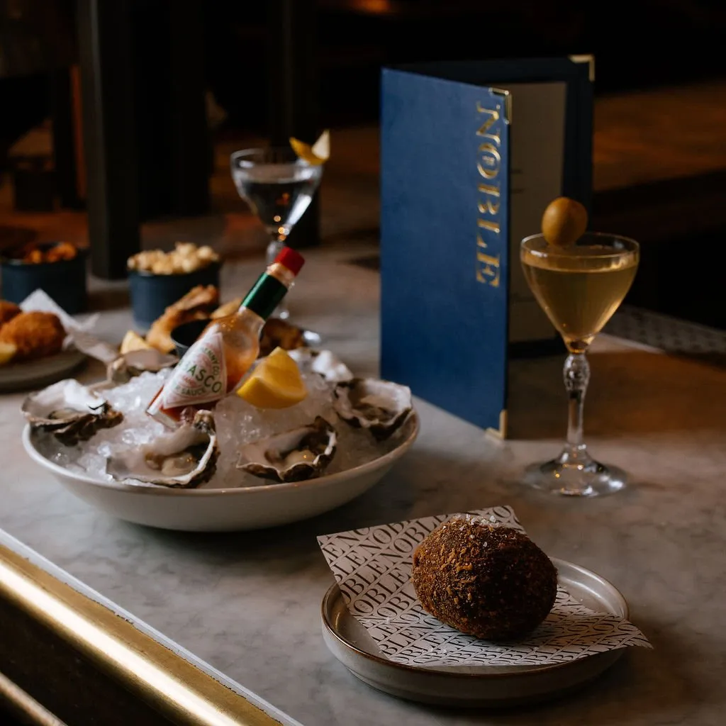 A close-up shot of a luxurious dining table setting featuring fresh oysters, cocktails, and a branded menu, highlighting the upscale culinary experience.