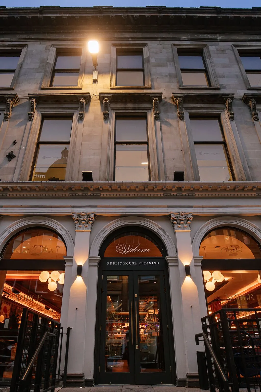An inviting low-angle exterior shot of a historic stone building's ground floor entrance, featuring a 'Public House & Dining' establishment illuminated by warm evening lights.