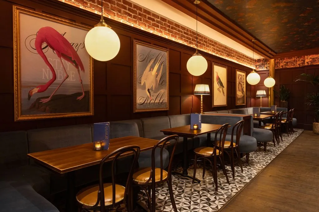 A cozy and sophisticated restaurant interior features dark wood paneling, plush navy banquette seating, and a striking geometric tiled floor, illuminated by warm ambient lighting.